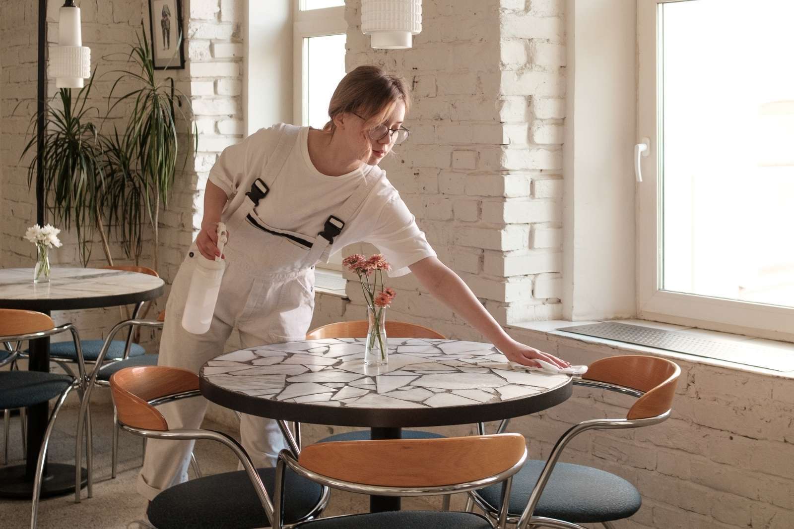 A server in white wipes down a white and black cafe table.