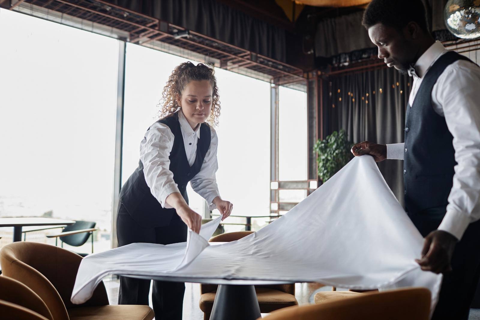 Restaurant staff setting out clean tablecloth 