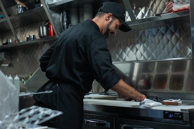 Food handler cleaning the kitchen to help prevent cross contamination