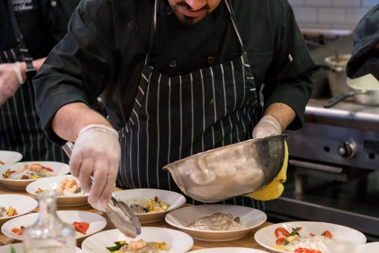 Food handler carefully plating dishes while wearing gloves