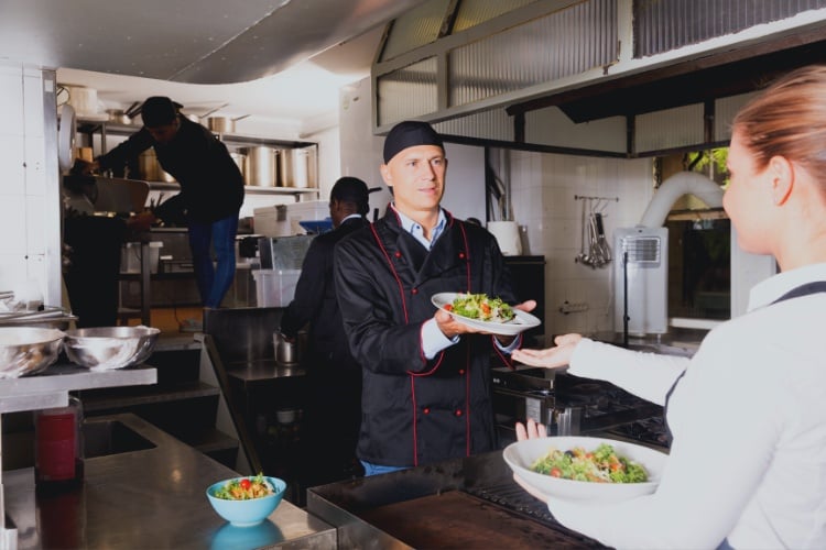 Chef handing a dish off to a server with proper food safety handling.