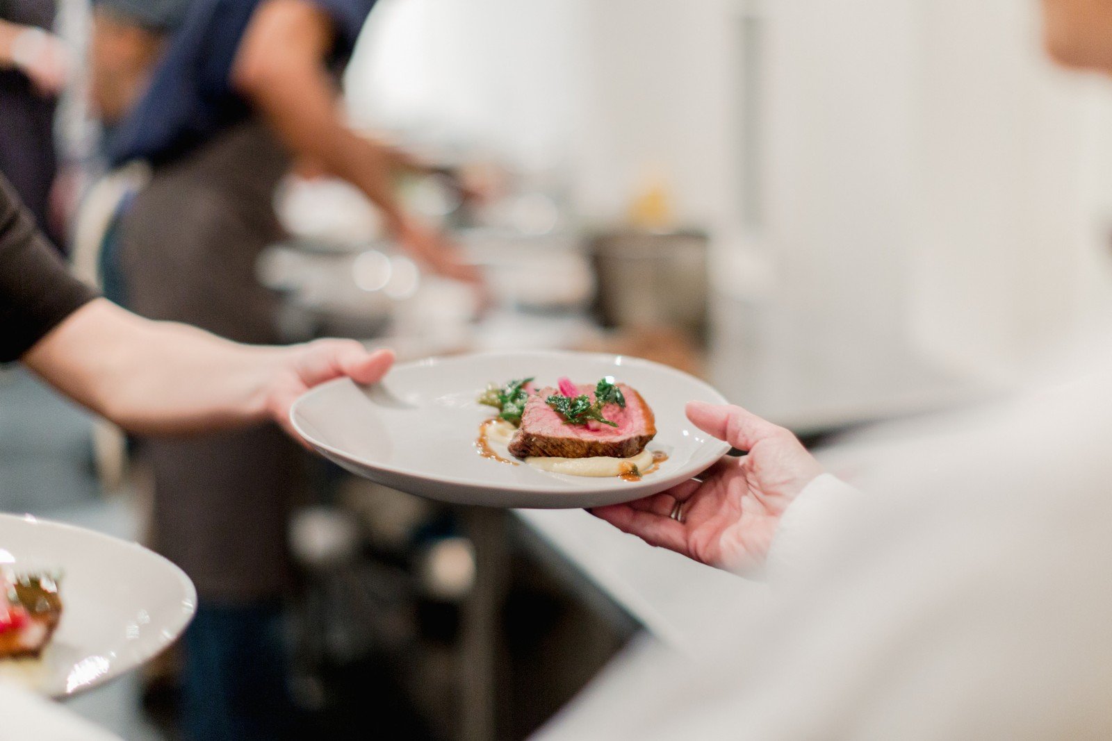 Food handler passing a meat dish to a server