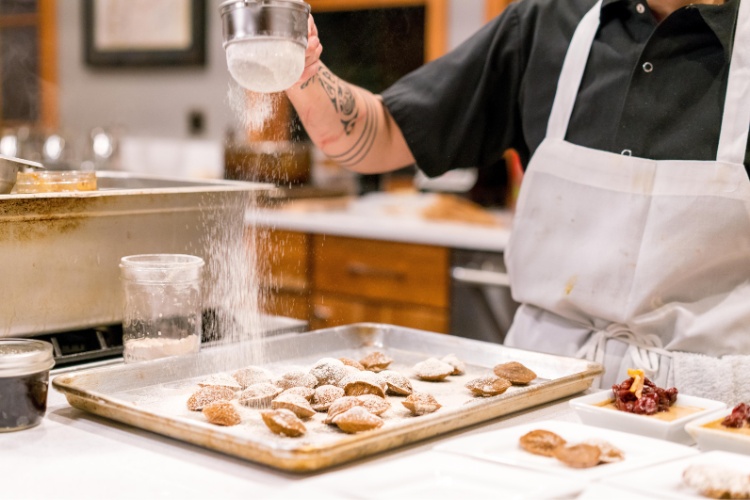 Food handler shaking powders sugar onto baked goods